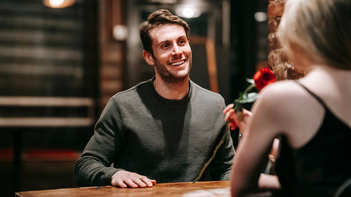 A man smiling at his date, who's sitting across the table and smelling a rose he gave her.