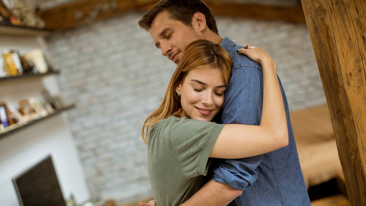 A couple hugging each other, eyes closed and smiling.