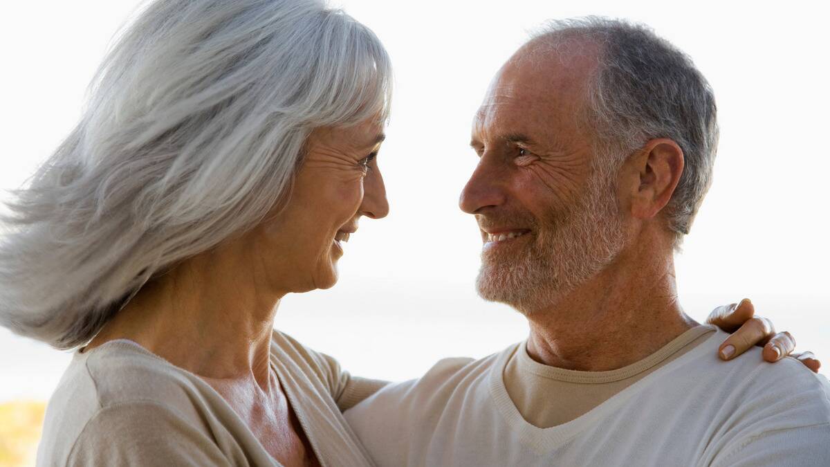 A couple standing close together, smiling as they look into each others eyes.