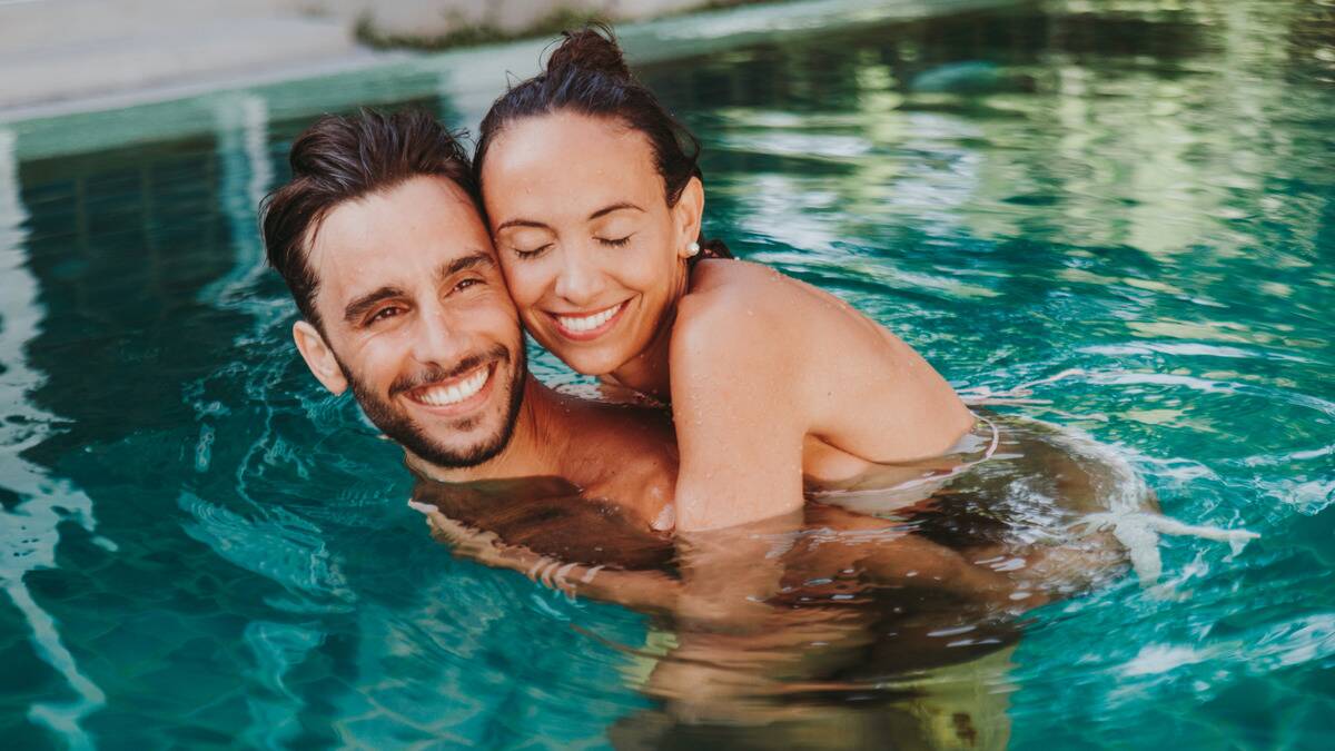 A couple in a pool together, the man giving the woman a piggyback ride.