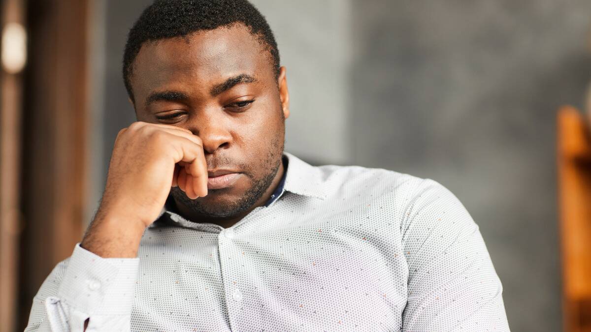 A close shot of a man sitting, hand on his face, looking sad or dissapointed.