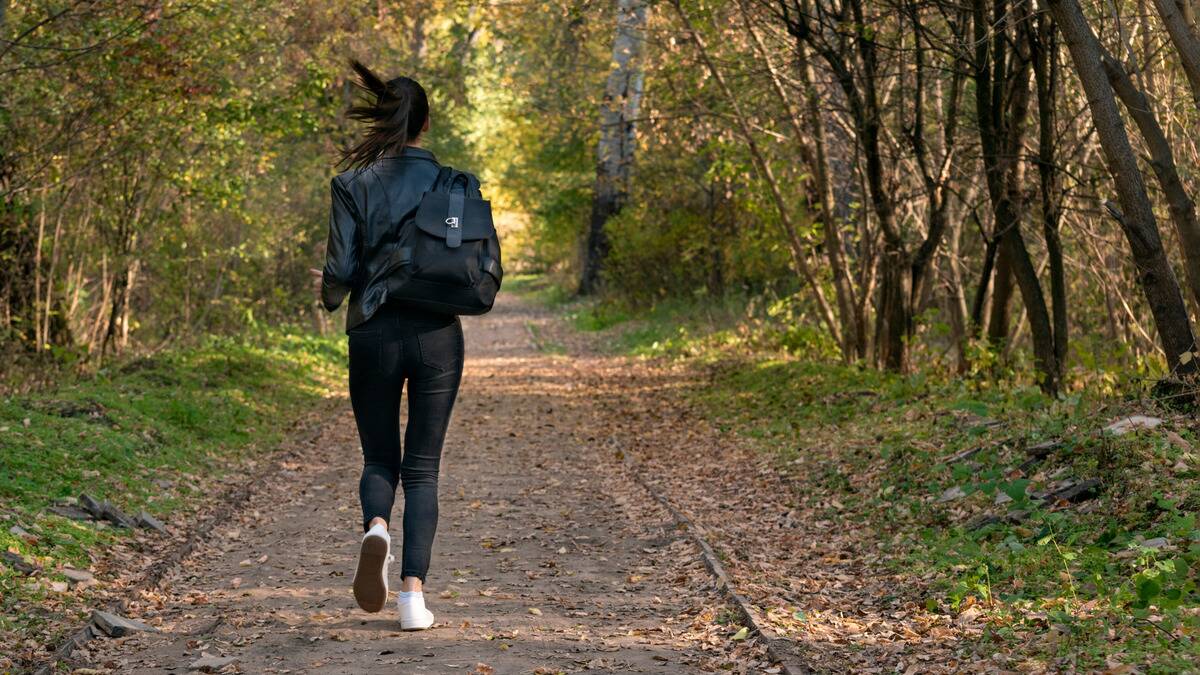 A woman running away from the camera down a paved path.