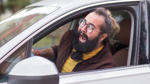 A man driving a car, sticking his head out the window and shouting.