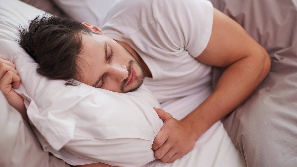 A man asleep on his side in bed, one hand holding the pillow.