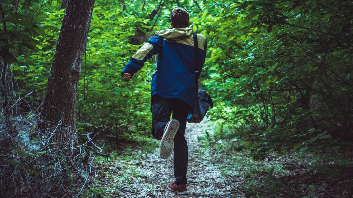 A man running away from the camera down a forest path.