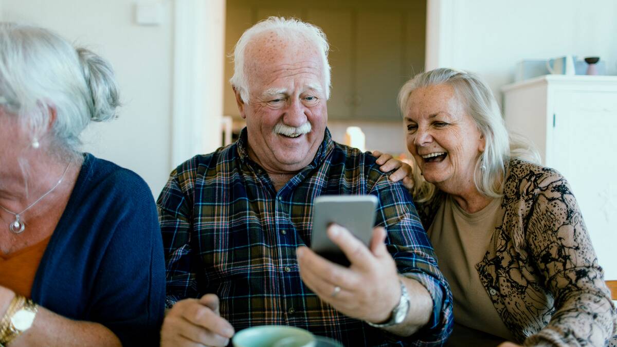 An older couple both smiling as they look at something on one of their cellphone's.