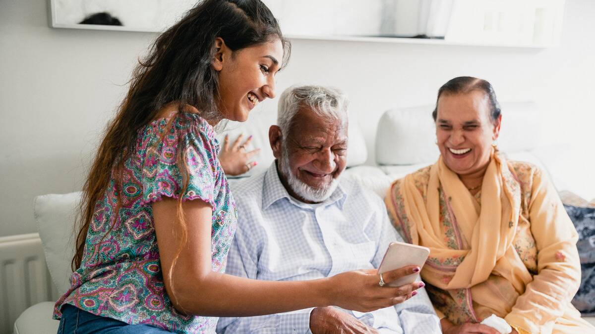 A daughter smiling with her parents as she shows them something on her phone.