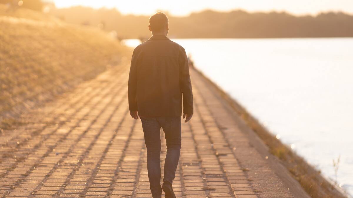 A man walking away from the camera down a brick road in the sunrise.