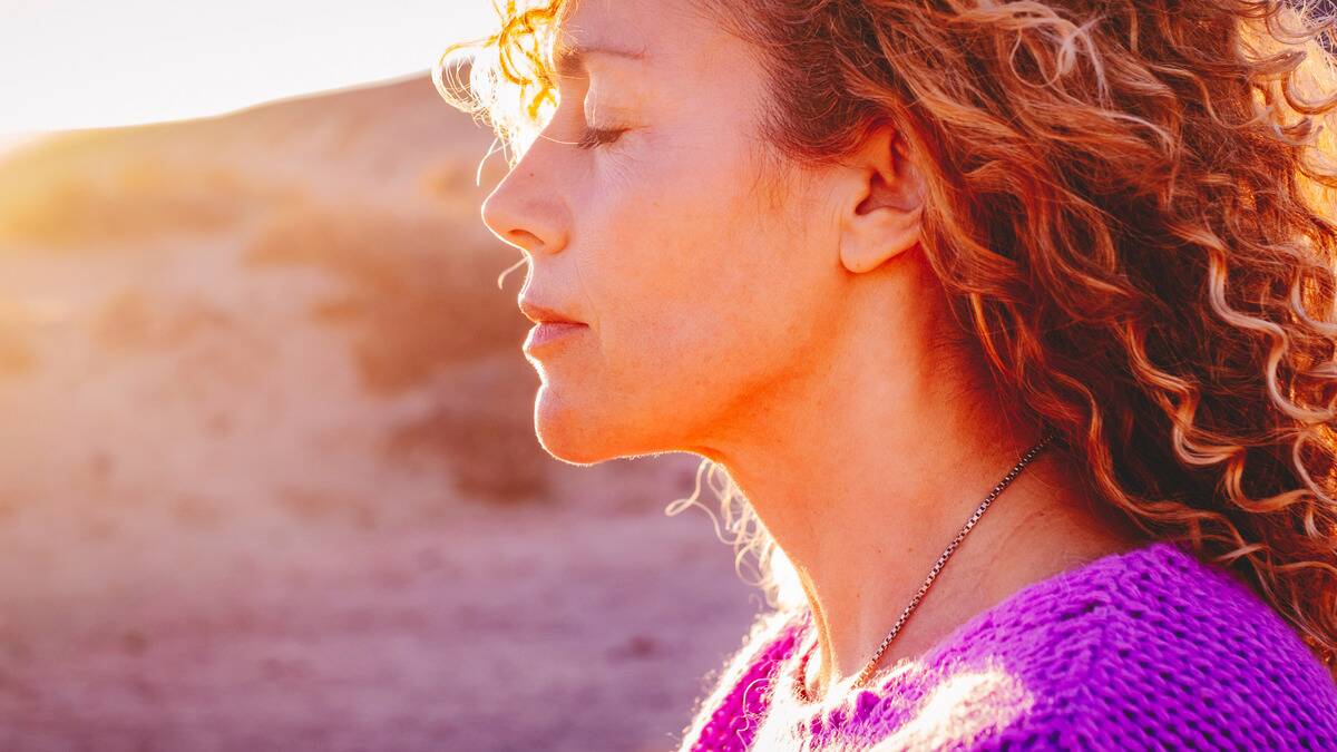 A close shot of a woman with her eyes closed peacefully in the sunshine.