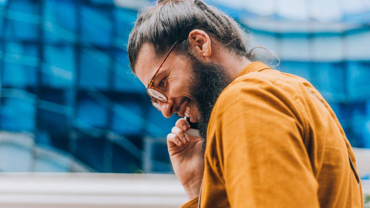 A close, low shot of a man smiling as he talks on his cellphone, holding it up to his ear.