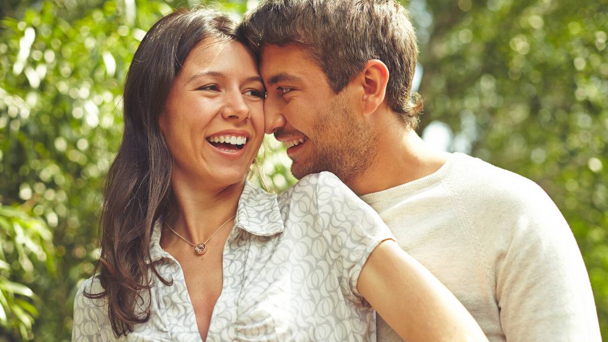 A couple standing close outdoors, the man pressing his forehead and nose into the side of the woman's head.