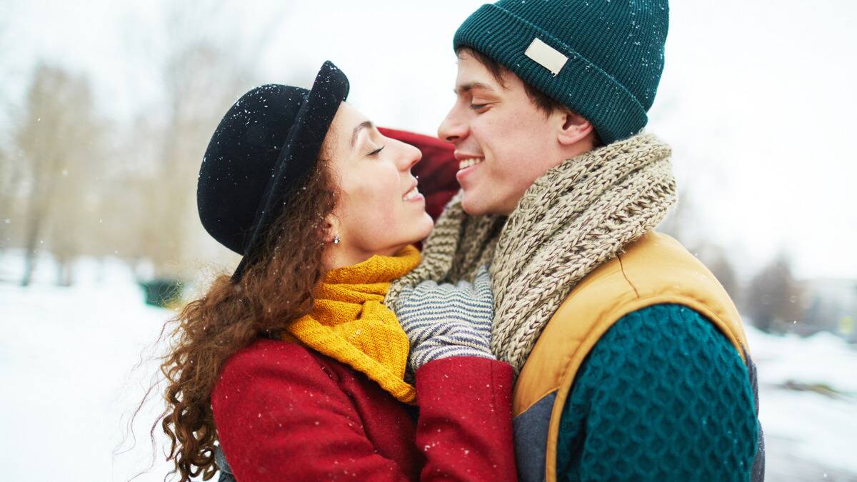 A couple in bright winter gear standing very close, smiling at each other in the snow.