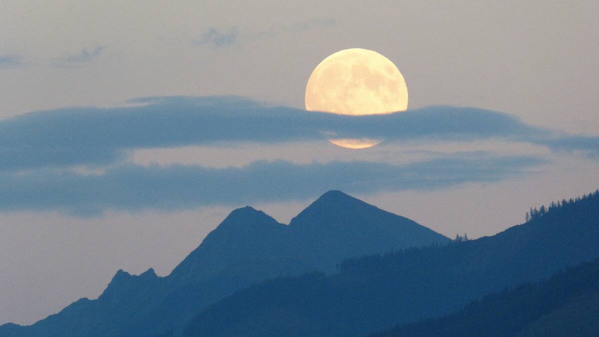 A large full moon in the sky above the silhouette of some mountains.