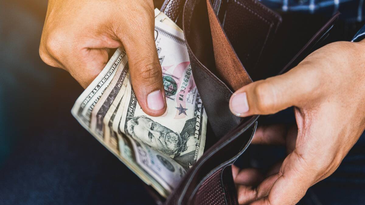 A close shot of someone pulling out a small stack of bills out of their wallet.