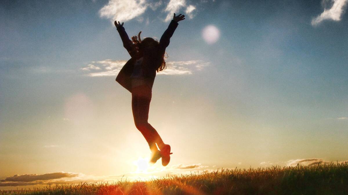 The silhouette of someone jumping in the air in joy as the sun rises.