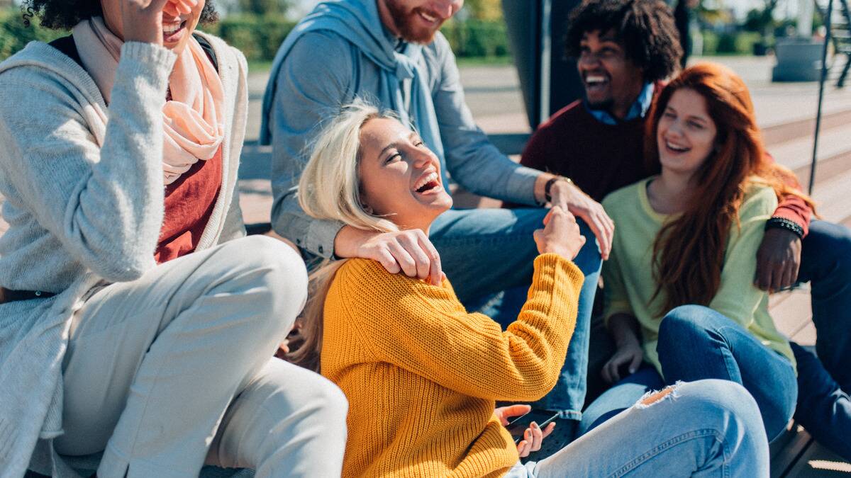 A group of friends sitting together outside, smiling and laughing as they talk.