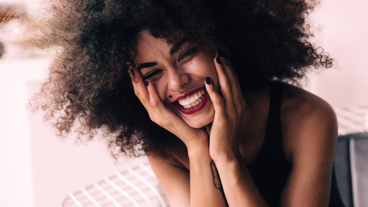 A close shot of a woman smiling, her hands on her cheeks.