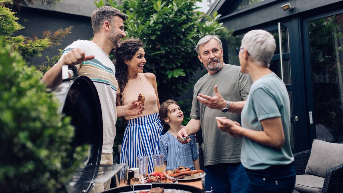 A family of a young daughter, her parents, and grandparents all chatting as they stand outside, having a barbecue.