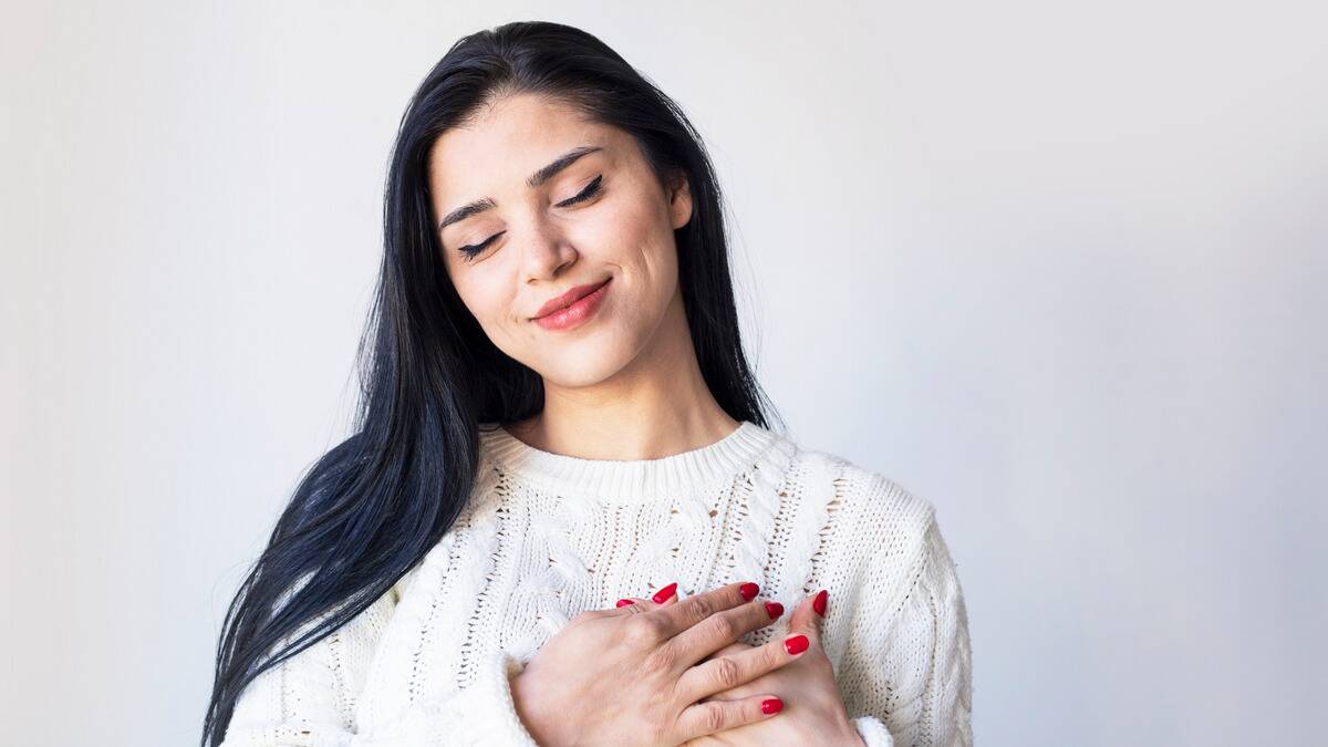 A woman smiling peacefully with her eyes closed, both hands over her heart.