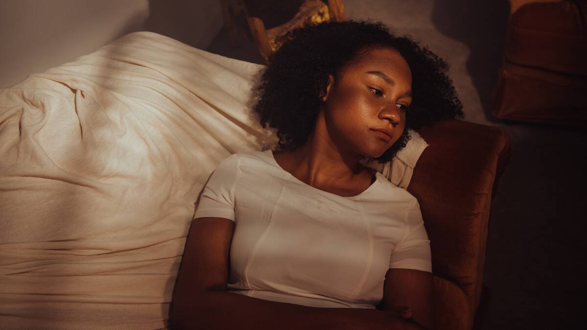 A woman laying on her couch with her arms folded, looking sad.