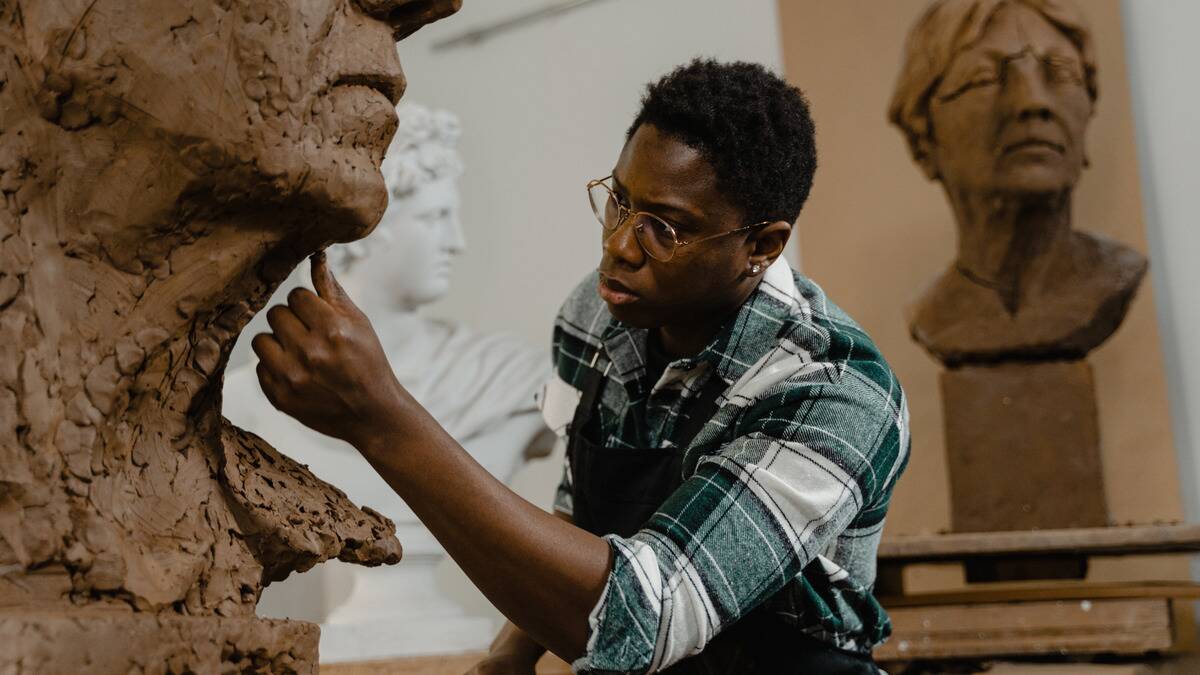 A man working on a large sculpture smoothing out parts with his hand, leaning close.