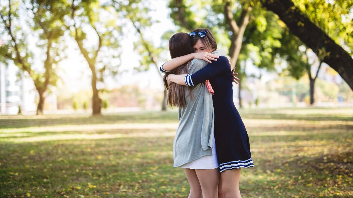 Two friends hugging outside, looking emotional.