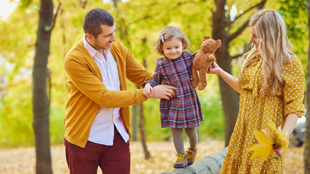 A mother and father helping their young daughter walk along and balance on a fallen tree trunk.