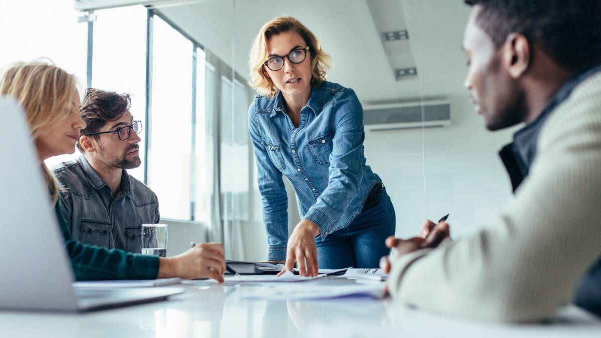 A low angle, table-height photo of a woman standing up as she leads a business meeting.