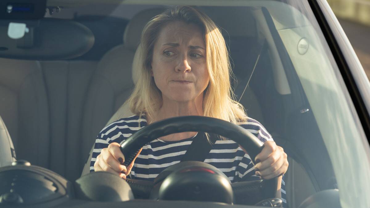 A woman sitting in the driver's seat of her car, looking stressed.