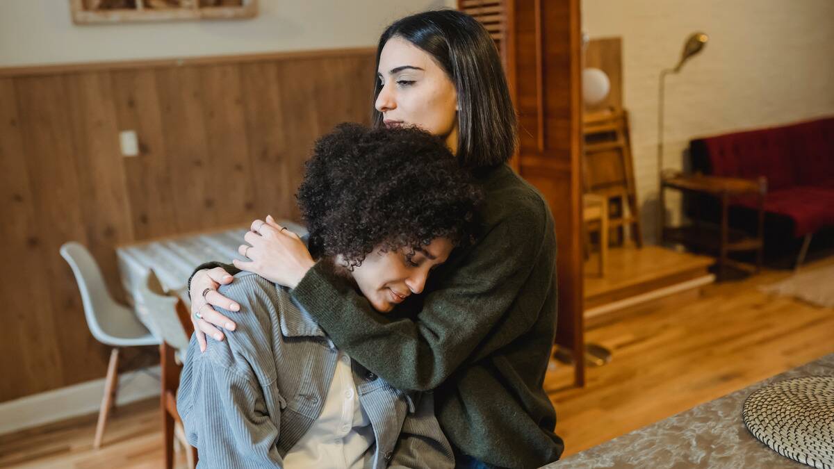 A woman holding her friend in an act of comfort, that friend smiling softly.