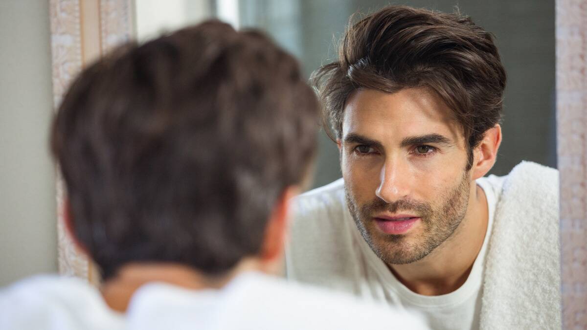 A close, over-the-shoulder shot of a man looking at himself in a mirror.