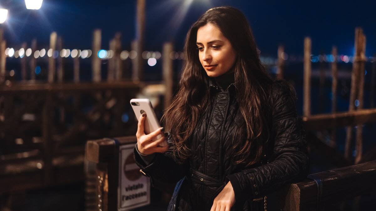 A woman smiling confidently as she looks at her phone while standing outside at night.