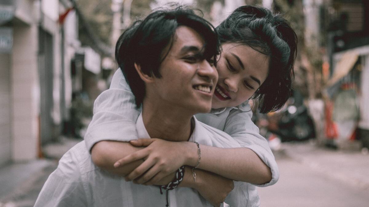 A couple walking down the street, the man giving the woman a piggyback ride, both smiling.