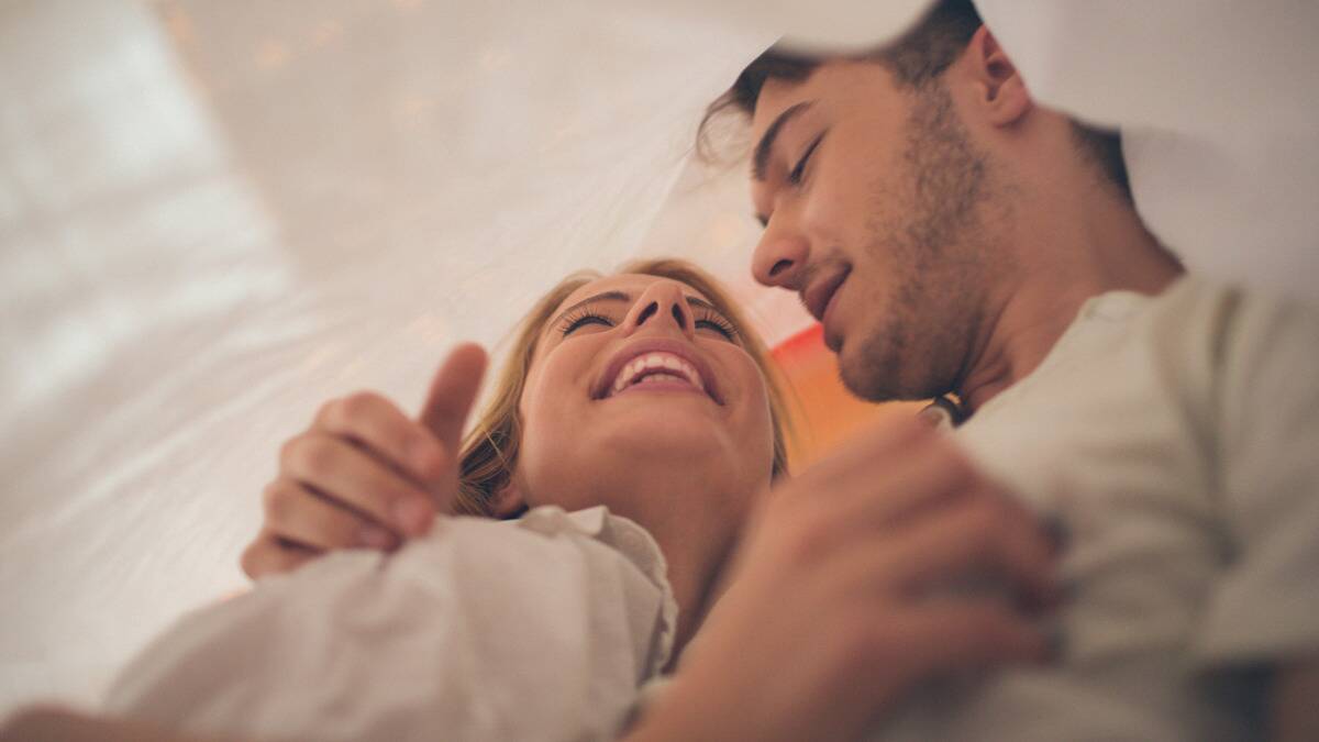 A close, low-angle shot of a couple under a sheet, laughing and hugging.