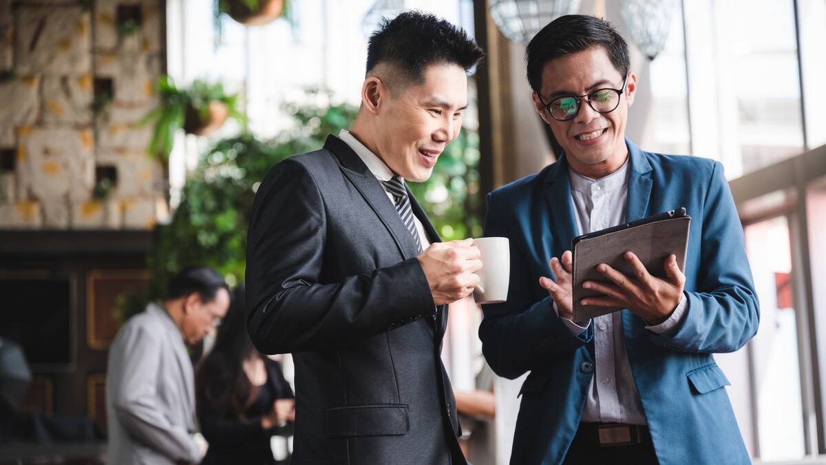 Two business partners chatting, one showing the other something on his tablet.