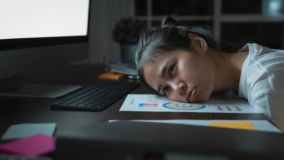 A woman laying her head on her work desk, looking sad.