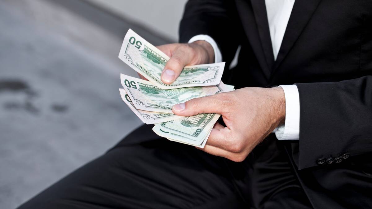 A close shot of someone in a suit counting a stack of $50 bills.