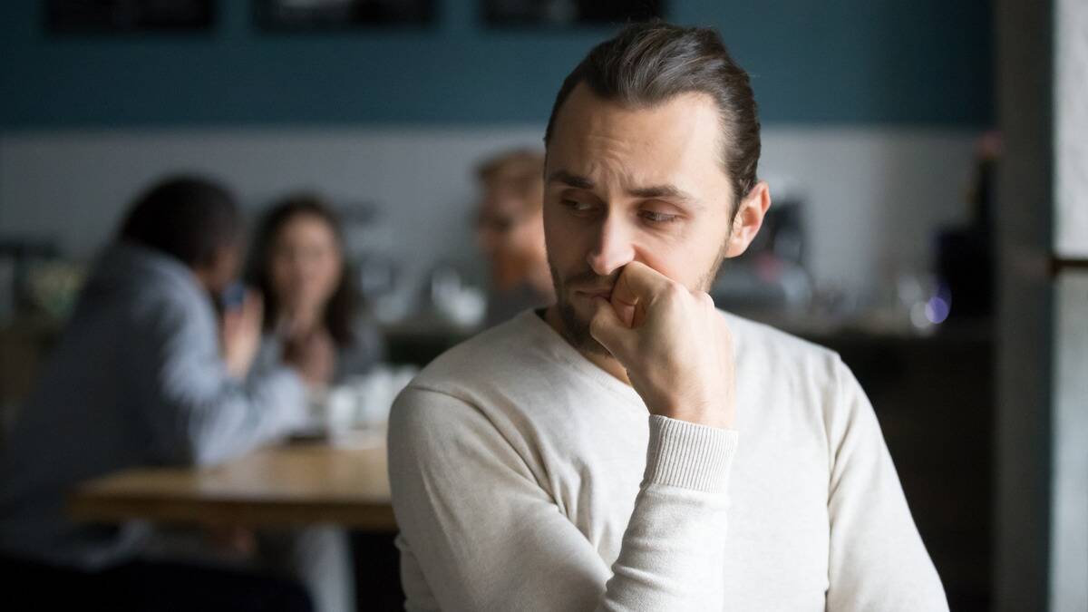 A man sitting at a table alone, nervously biting his nails, looking insecure.