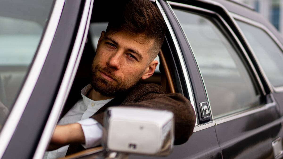 A confident, cocky man leaning out a car window.