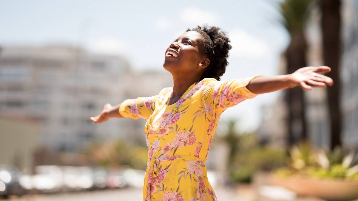 A woman standing outside, arms outstretched, looking upward, smiling brightly.