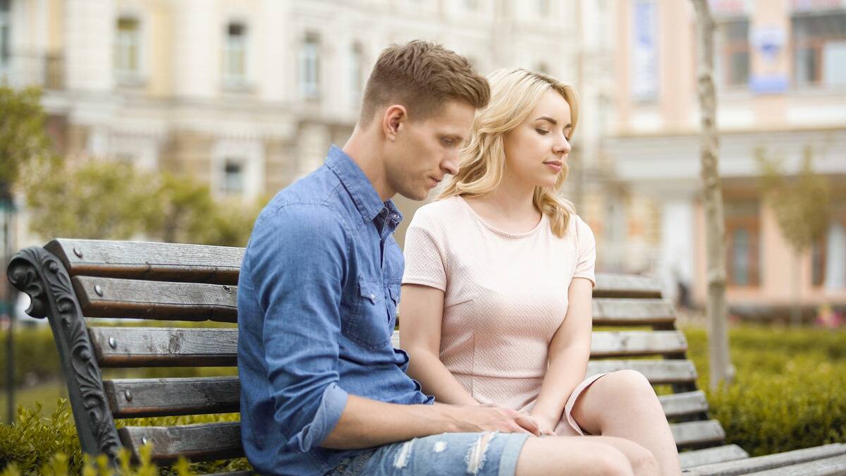 A couple sitting on a bench, both looking dejected and a bit awkward.