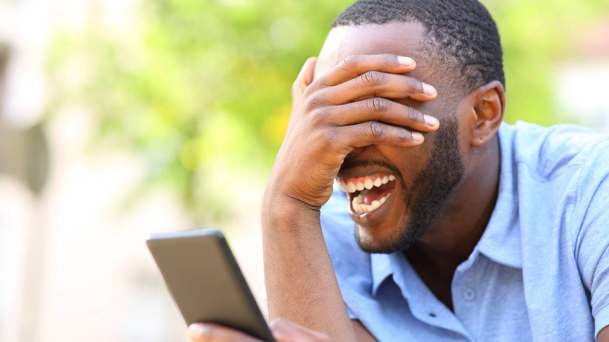 A man laughing so hard at something on his phone that he's covering his eyes.