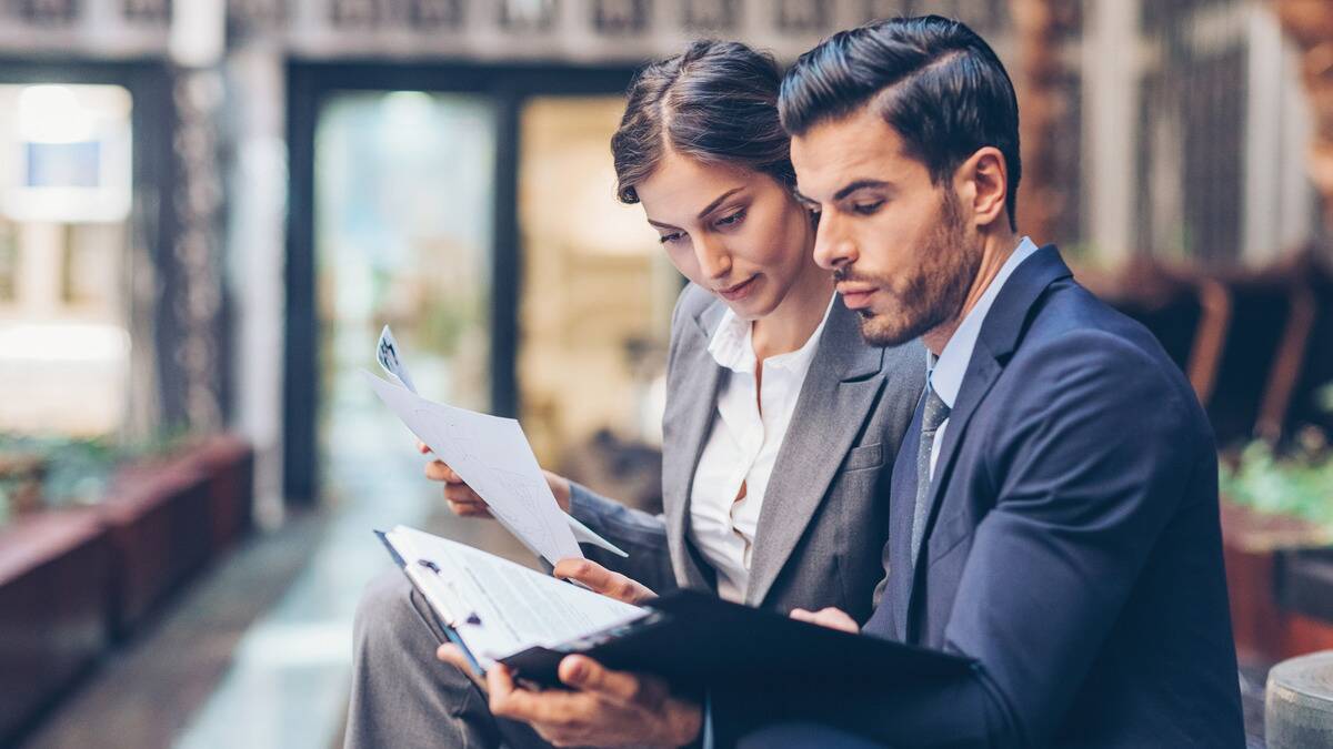 Two business people sitting side by side, comparing printed documents.