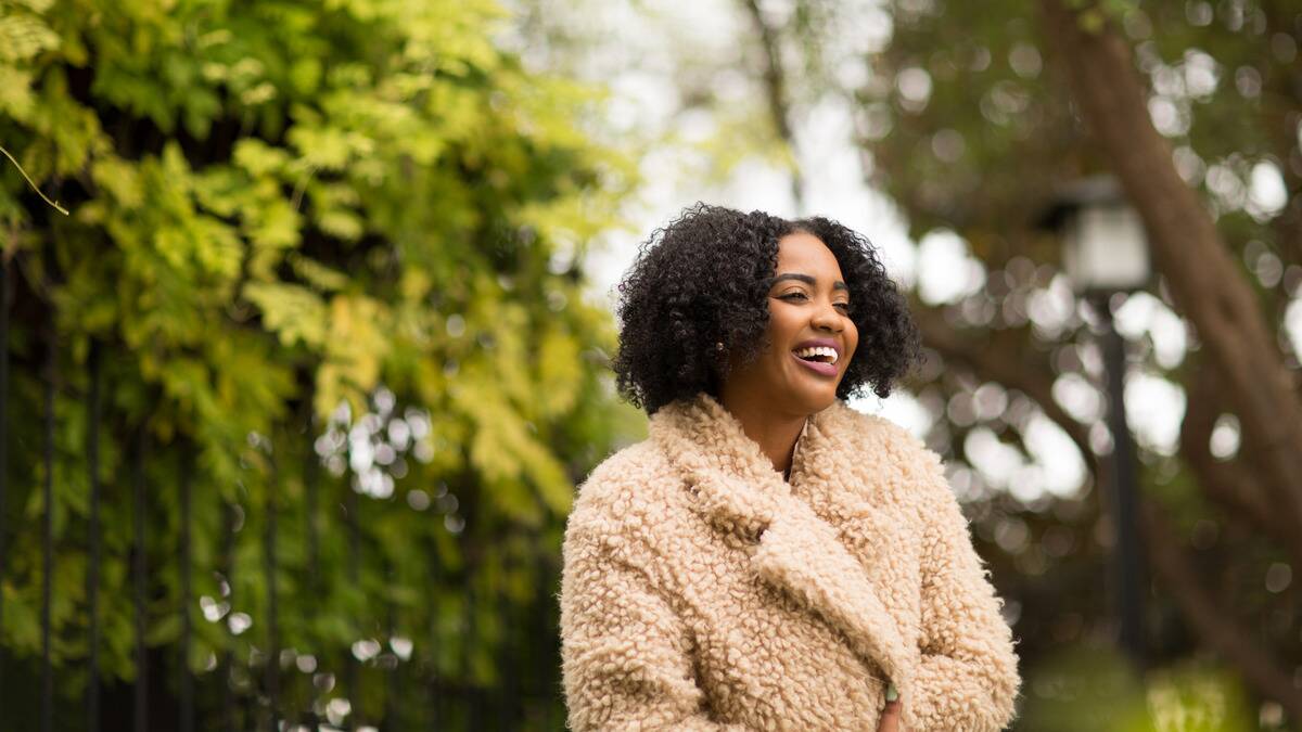 A woman standing outside in a fuzzy coat, smiling.