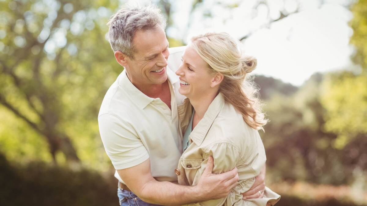 A couple hugging enthusiastically while standing out in the sun, smiling at each other.