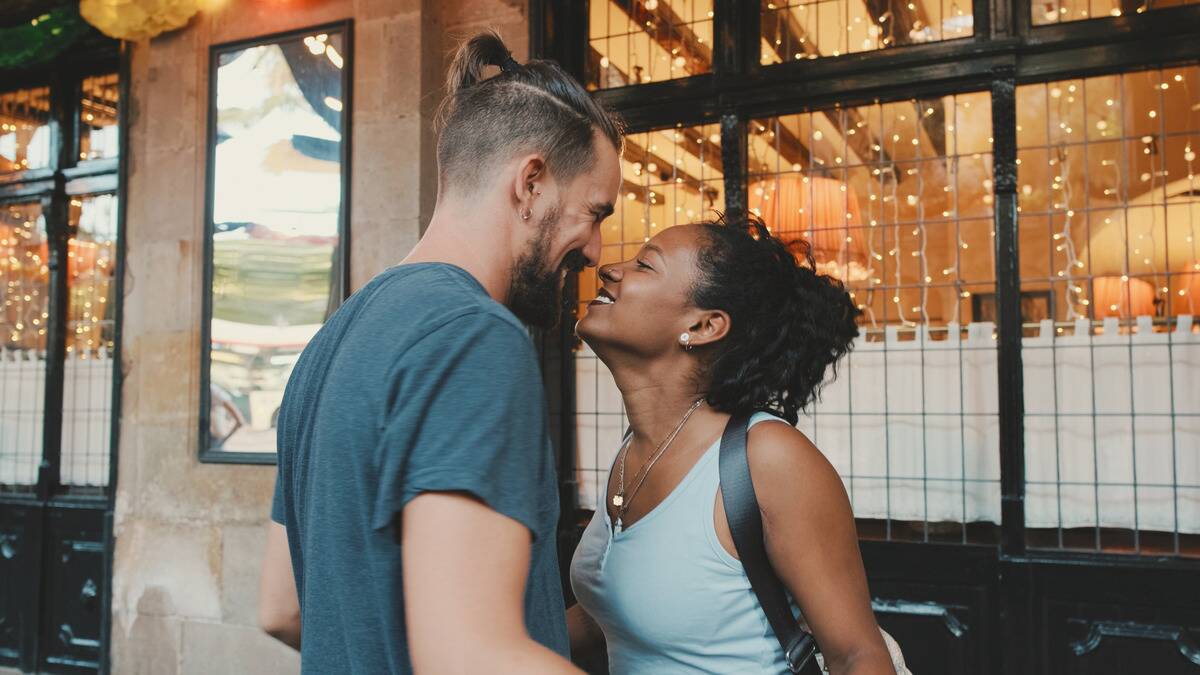 A couple standing close, the woman leaning up so their noses are barely touching.