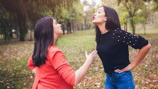 Two women arguing as they stand outside in a park.