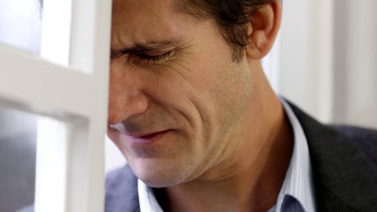 A closeup shot of a man resting his forehead against a door frame, looking pained.