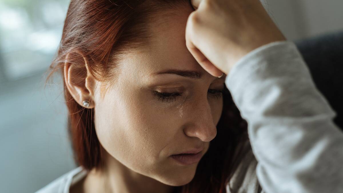 A closeup shot of a woman with a hand on her forehead, a tear on her cheek.