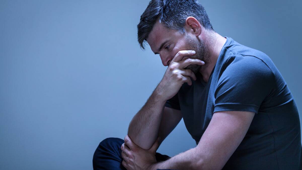 A man sitting, one leg folded, elbow on his knee, covering his mouth.